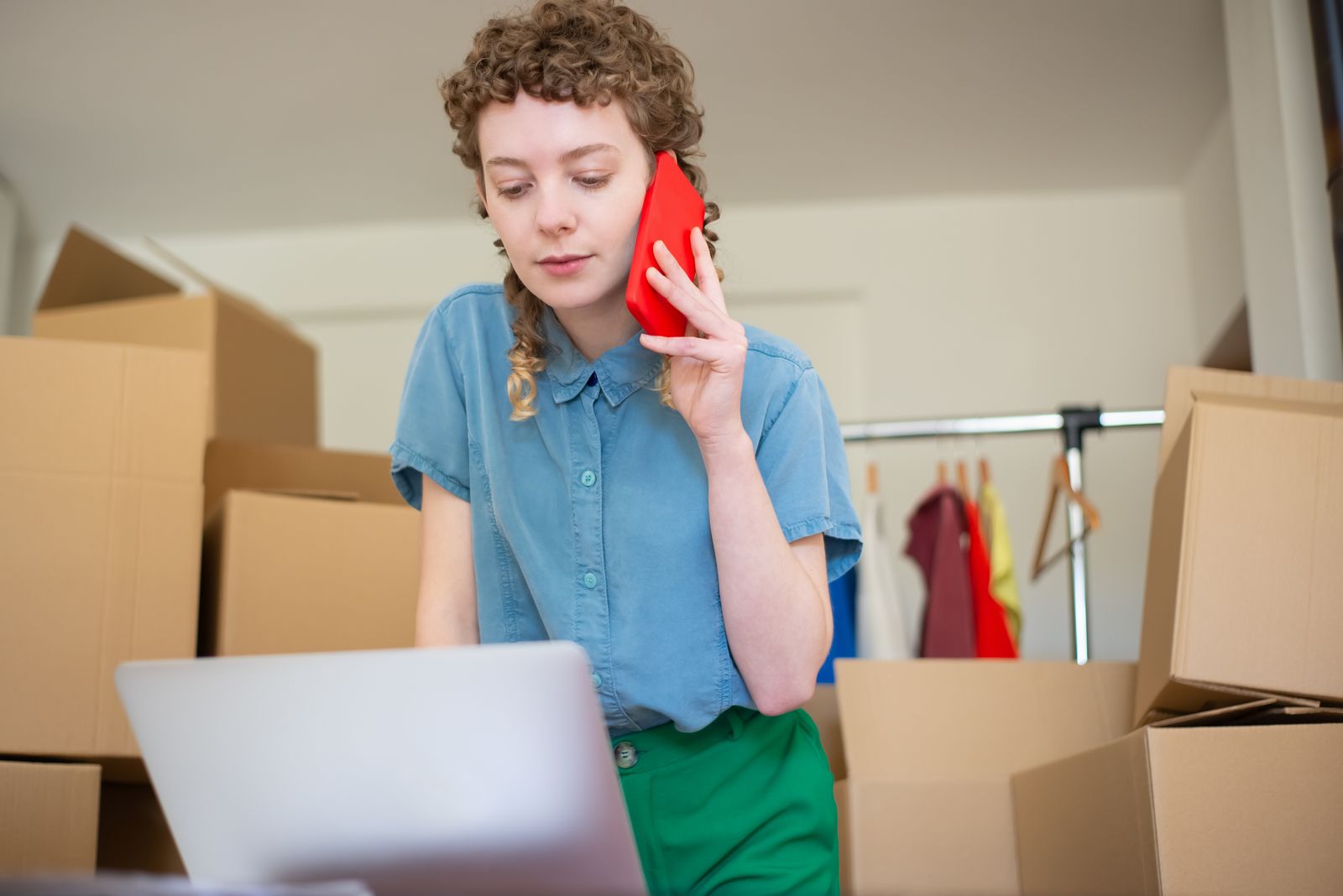 A small business owner on a phone call at a laptop, surrounded by packed boxes.
